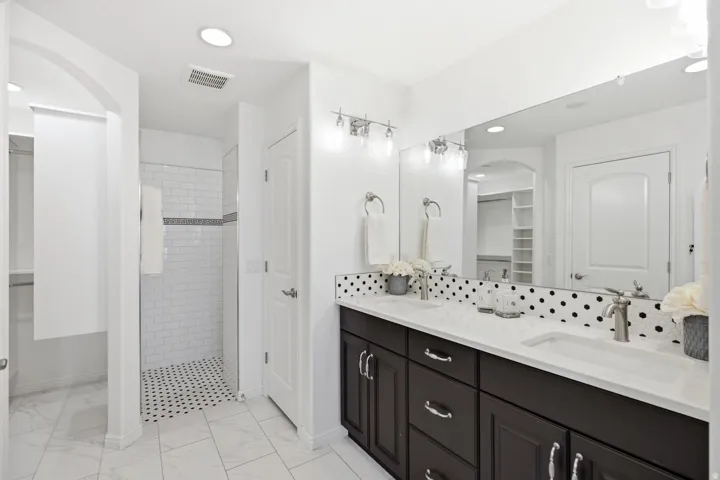 Spa-inspired primary bathroom featuring a dual-sink vanity with black cabinetry, white quartz countertop, and polished chrome hardware