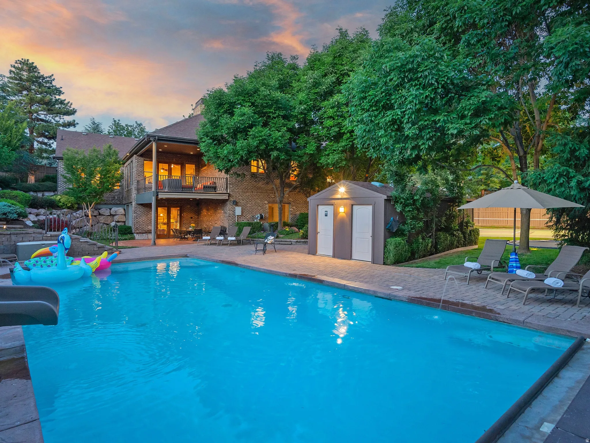 Swimming pool with integrated slide, brick paver patio, a dedicated pool house, and mature landscaping