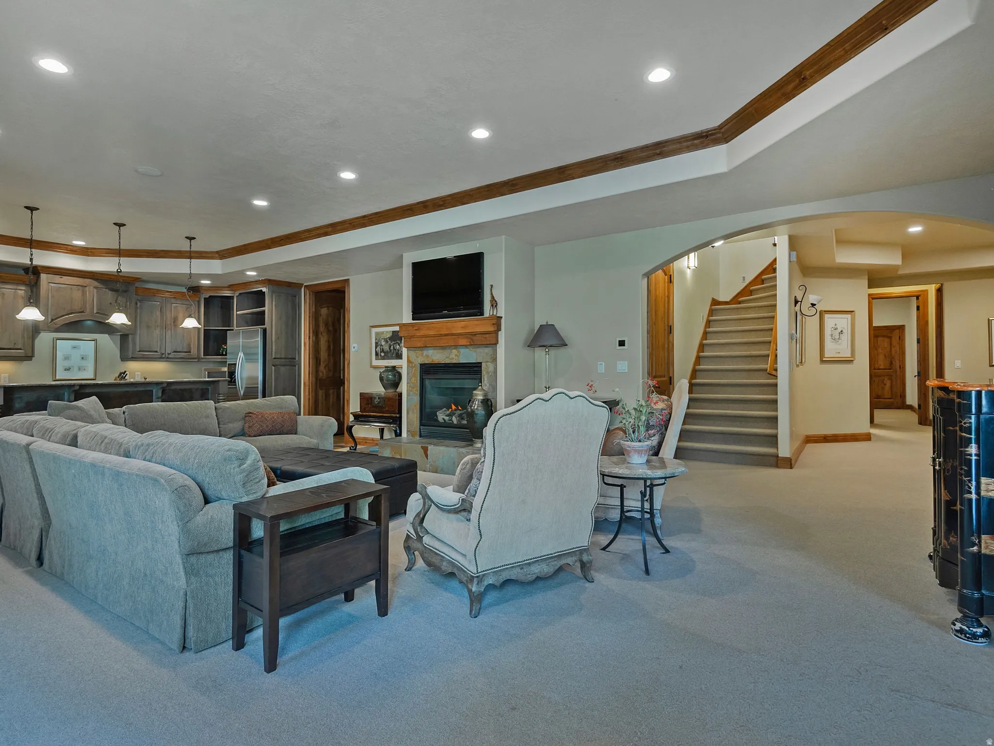 Integrated living space featuring a stone fireplace with a wood mantle, a built-in wet bar with cabinetry, recessed lighting, and a staircase with wood newel posts and handrail