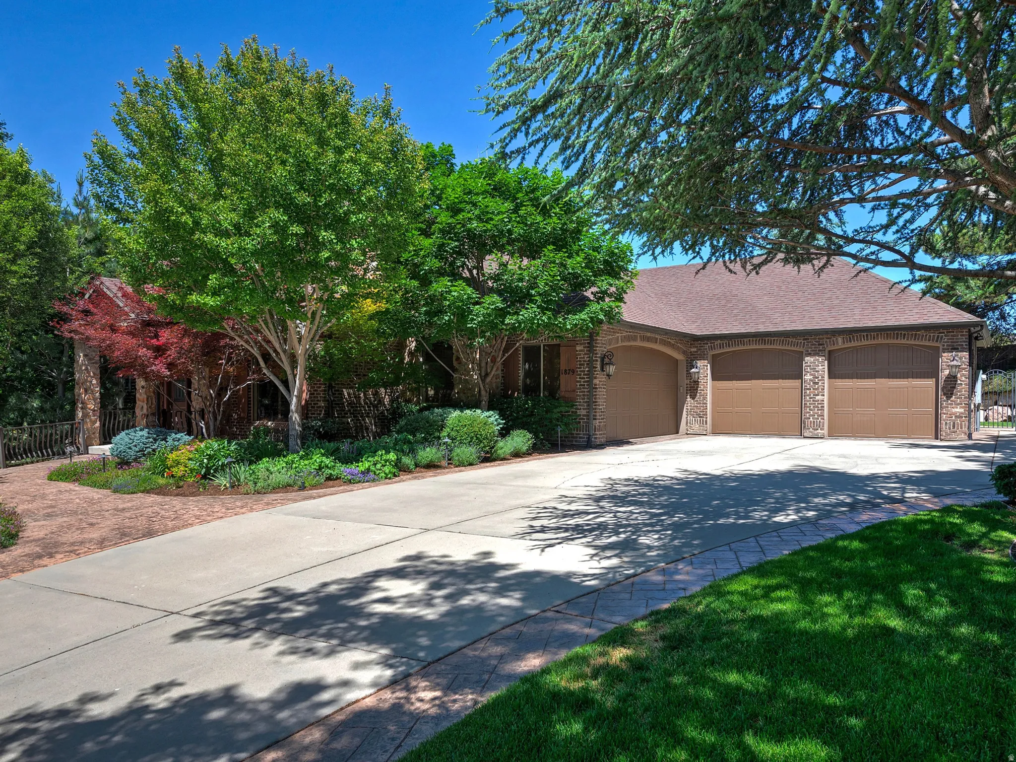 Brick exterior with a Four-car garage, concrete driveway, and mature landscaping