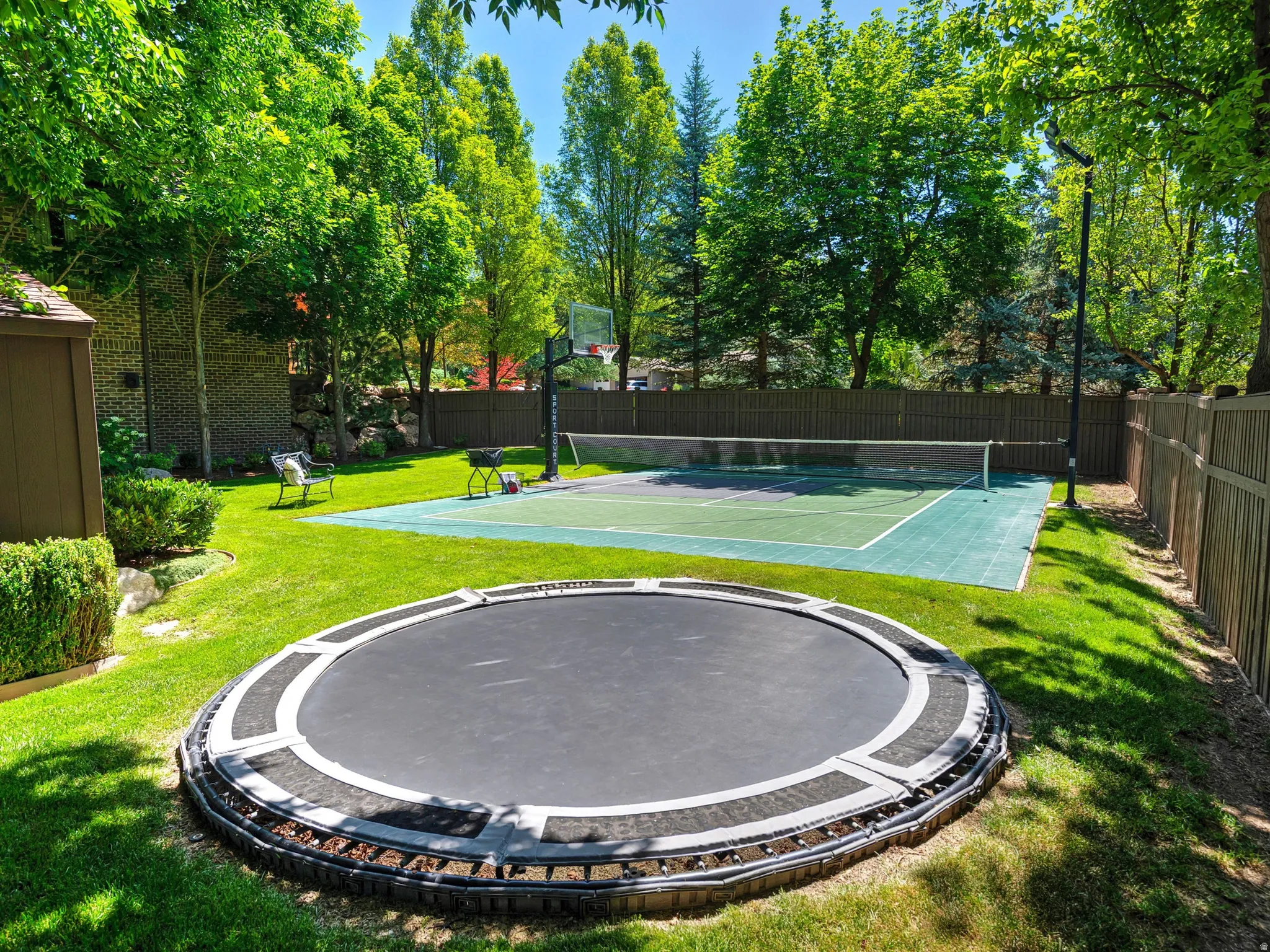 Expansive backyard featuring a manicured lawn, full-size sports court, and mature trees
