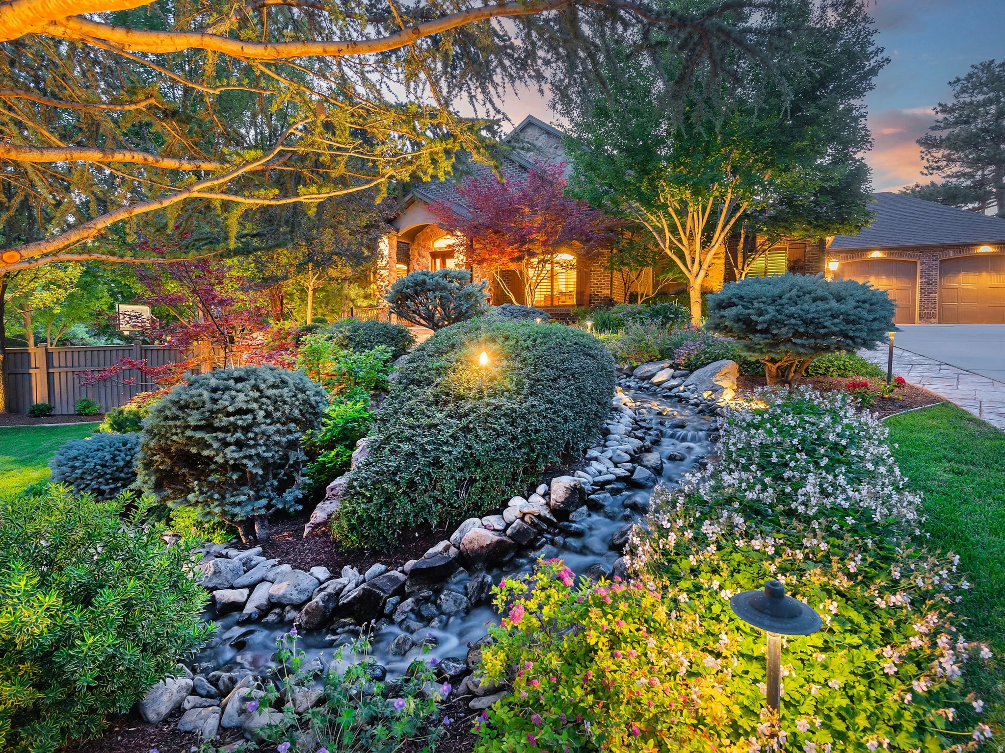 Manicured landscaping featuring a rock-lined stream, mature trees, and flowering shrubs