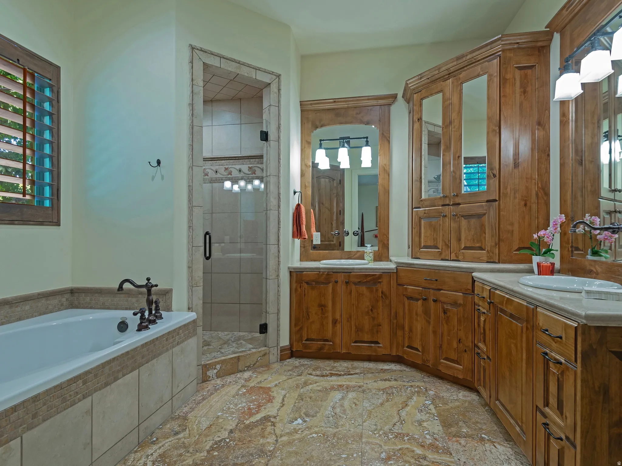 Dual vanity sinks with wood cabinetry, a built-in shower with tile surround, a soaking tub with tile surround, and tile flooring
