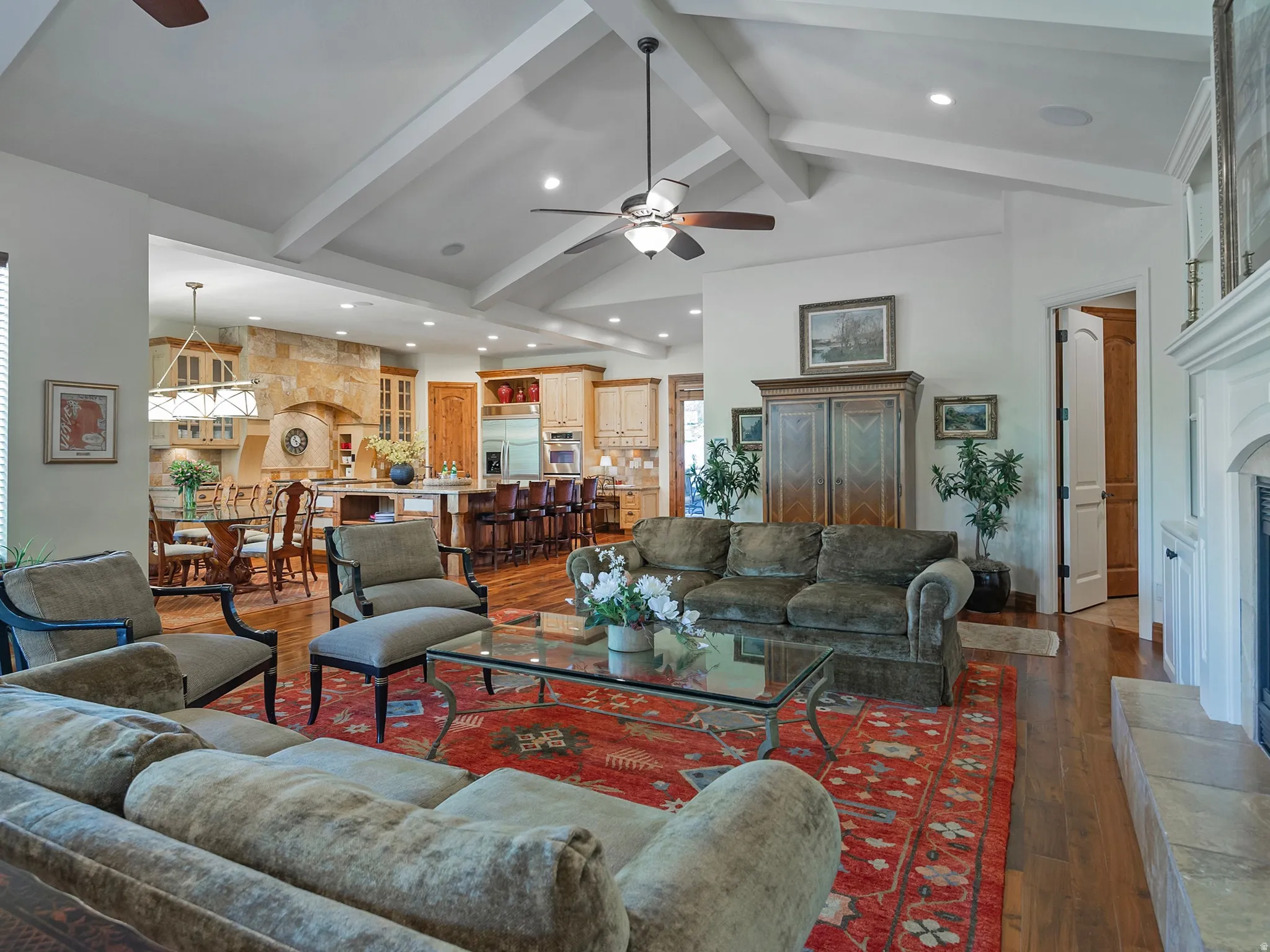 Vaulted ceilings with exposed beams, wood-finish flooring, a stone fireplace, and built-in kitchen cabinetry
