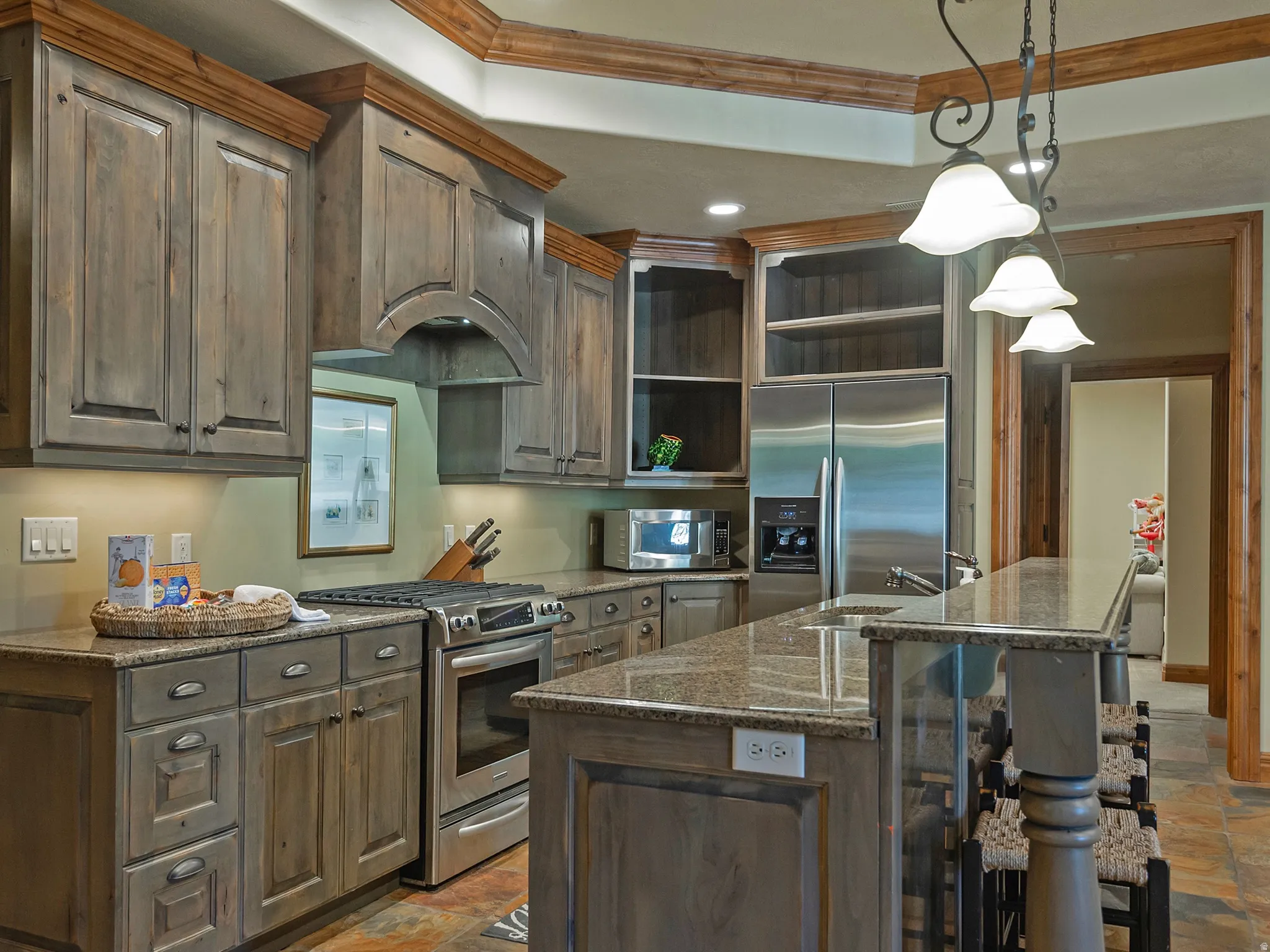 Distressed wood-finish cabinetry with crown molding, stainless steel appliances, granite countertops, and a multi-level island with seating