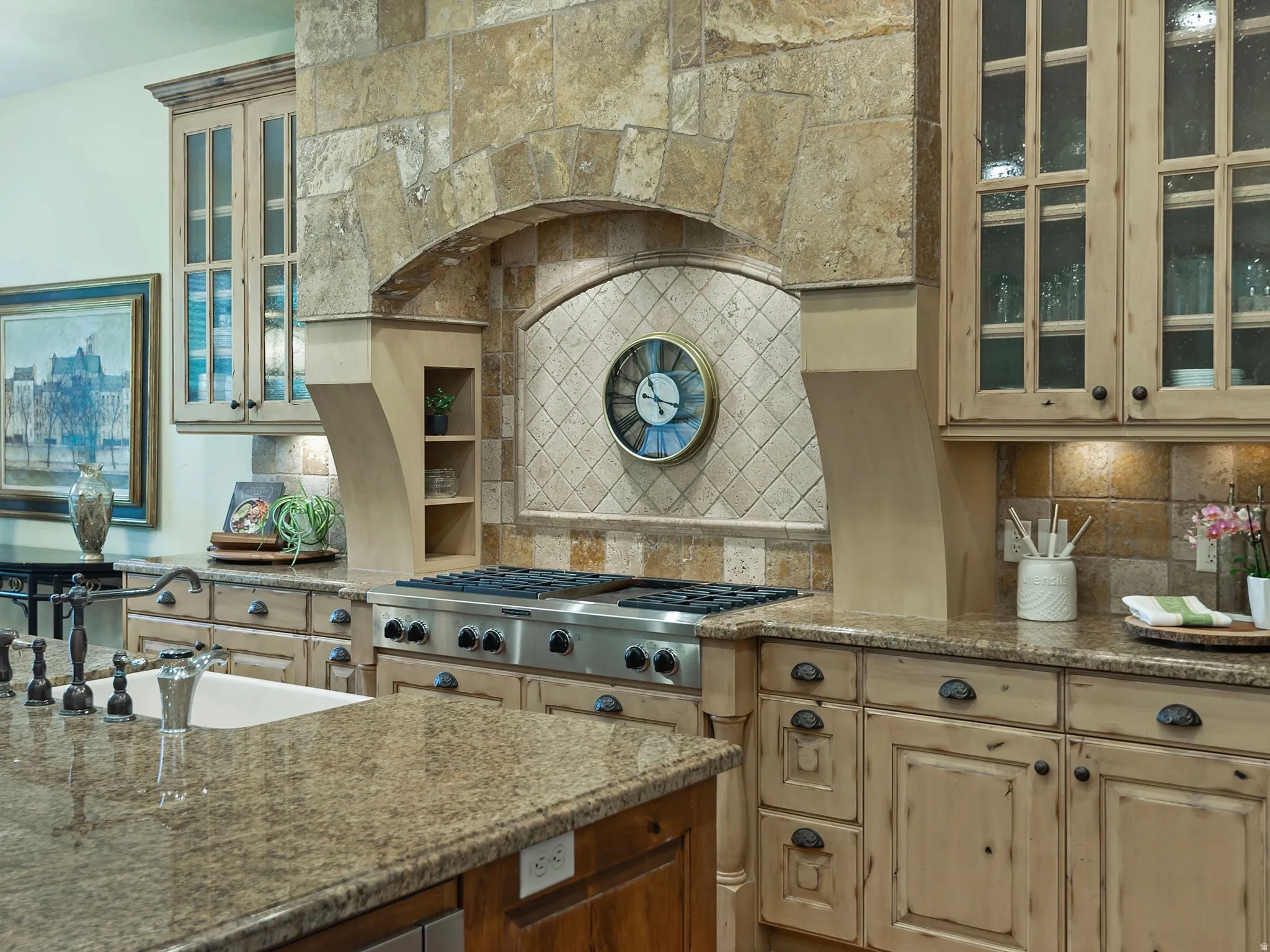 Gourmet kitchen featuring stone-clad range hood, professional-grade stainless steel gas range, stone tile backsplash, wood-finish cabinetry with glass inserts, and stone countertops