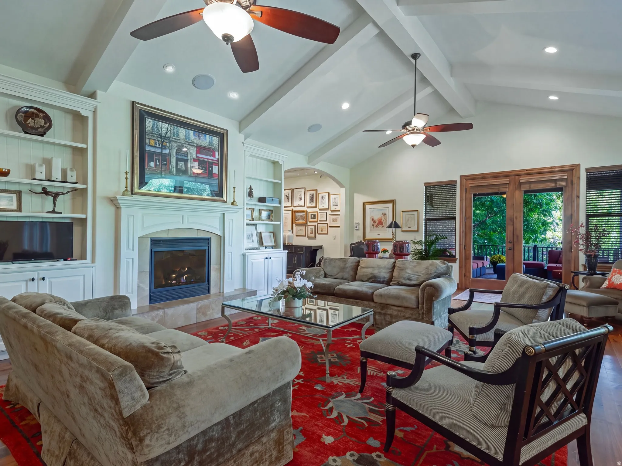 Vaulted ceiling with exposed beams, central fireplace, built-in cabinetry, wood-finish flooring, and French doors to the exterior