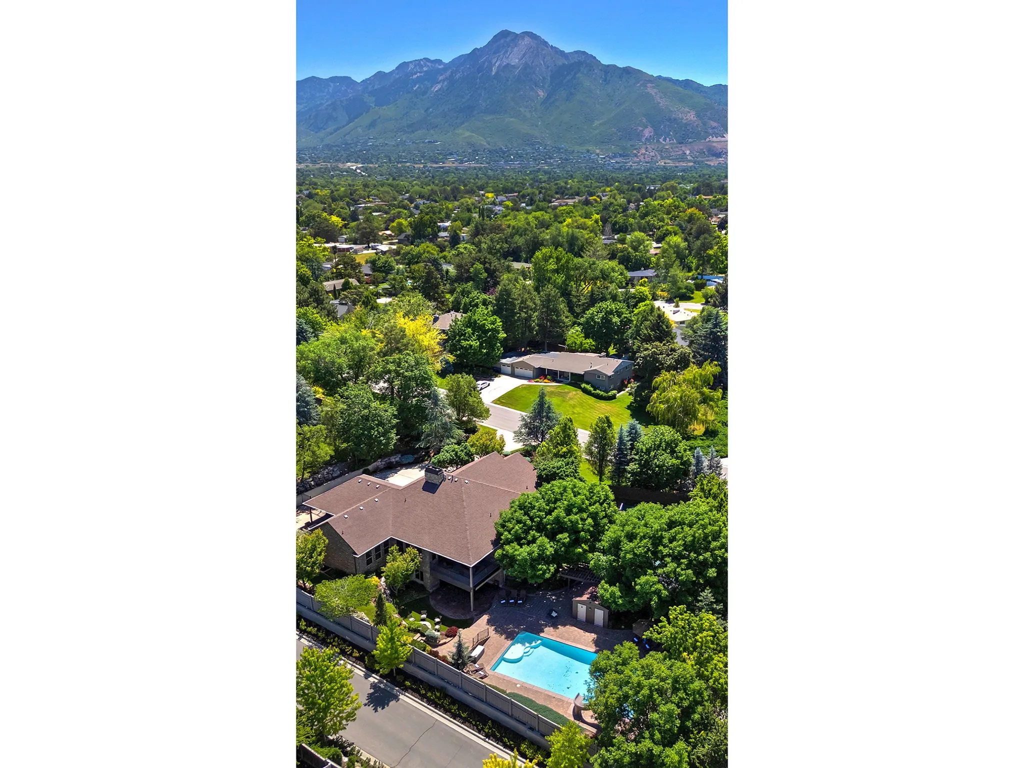 Aerial overview featuring mature trees, a swimming pool, and a mountain backdrop