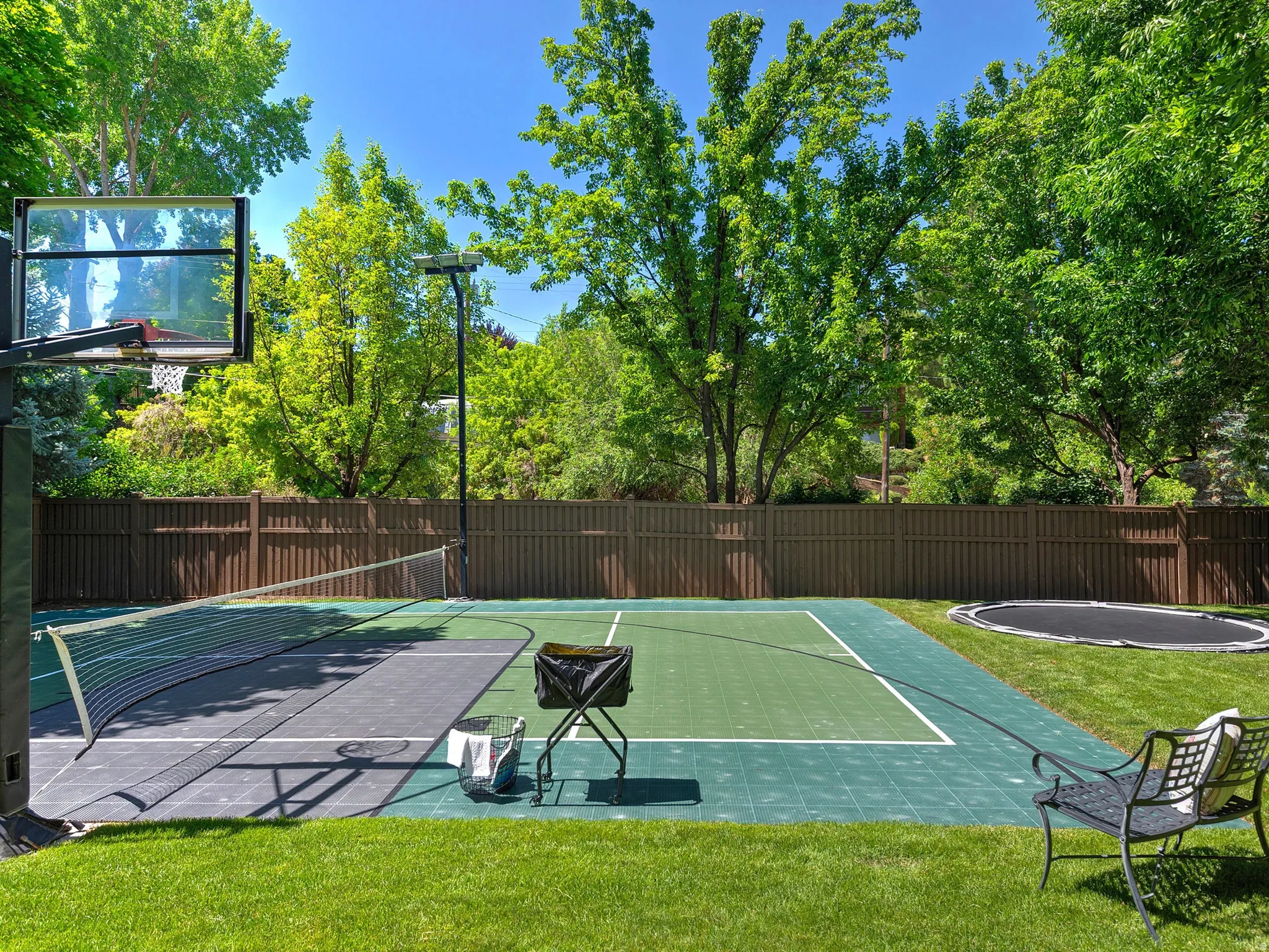 Manicured lawn with a multi-sport court, basketball hoop, and privacy fencing