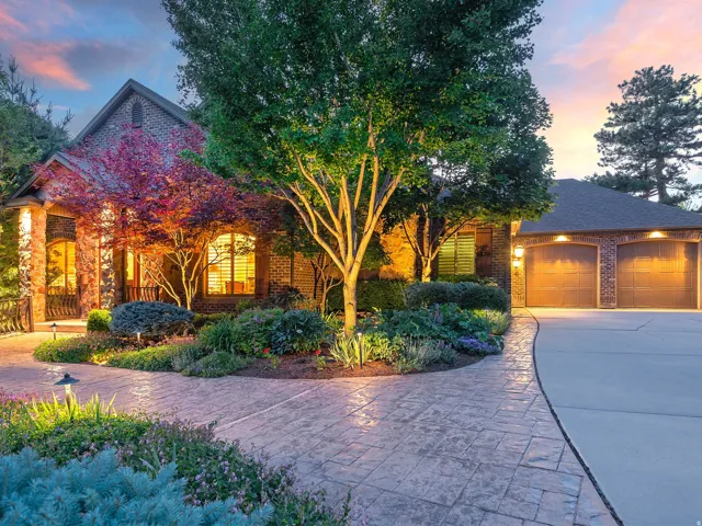 Stone and brick exterior with a gabled roofline, stamped concrete walkway, mature landscaping, and a multi-car garage