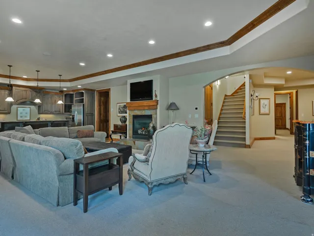 Integrated living space featuring a stone fireplace with a wood mantle, a built-in wet bar with cabinetry, recessed lighting, and a staircase with wood newel posts and handrail