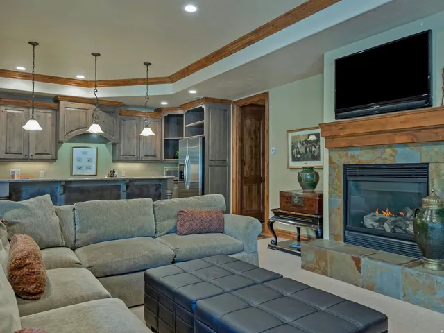 Stone-clad fireplace with a wood mantel, overhead recessed lighting, three pendant lights, wood-finish cabinetry, and a built-in bar, Kitchen area