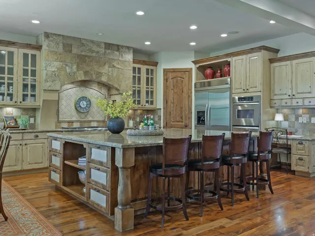 Expansive kitchen featuring a large island with seating, stainless steel appliances, stone-clad range hood, wood-finish flooring, and custom cabinetry