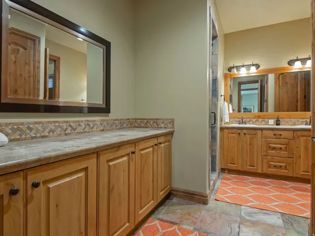 Dual wood-finish vanities with undermount sinks, stone countertops, and full mirrors