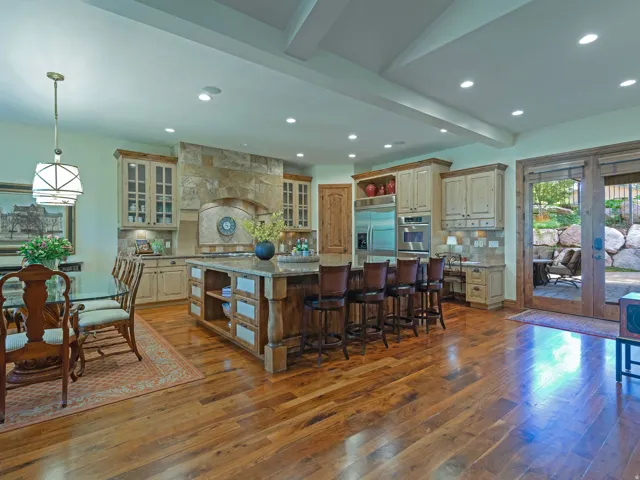 Hardwood flooring throughout, a central kitchen island with seating, stone-clad range hood, stainless steel appliances, and glass-paneled patio doors