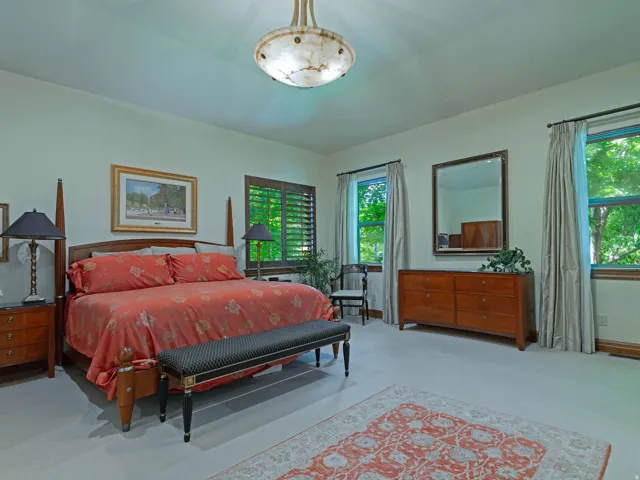 Plush carpeting, a prominent ceiling fixture, and multiple windows with plantation shutters and drapes