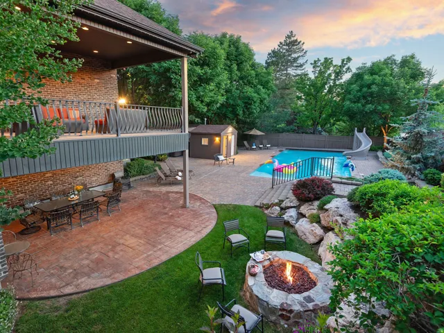 Expansive backyard featuring a patio with stamped concrete, a stone fire pit, a swimming pool with a slide, mature landscaping, and a multi-level deck