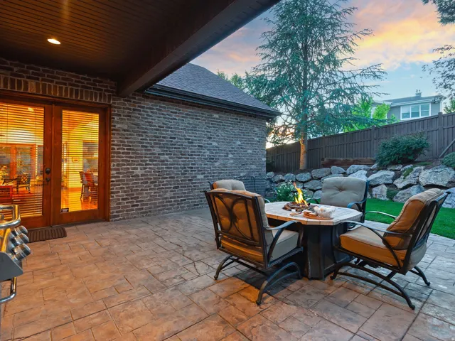 Stained concrete patio with an integrated fire pit, brick exterior, and a rock retaining wall