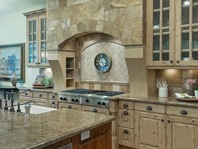 Gourmet kitchen featuring stone-clad range hood, professional-grade stainless steel gas range, stone tile backsplash, wood-finish cabinetry with glass inserts, and stone countertops