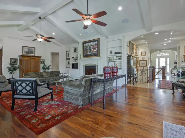 Vaulted ceiling with exposed beams, wood-finish flooring, built-in shelving, fireplace with mantel, and ceiling fans