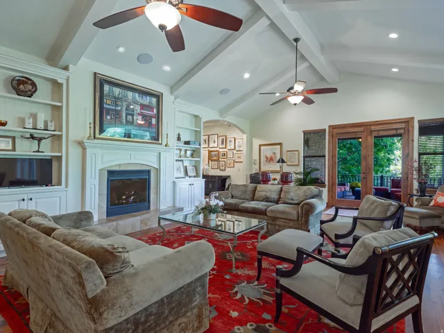 Vaulted ceiling with exposed beams, central fireplace, built-in cabinetry, wood-finish flooring, and French doors to the exterior