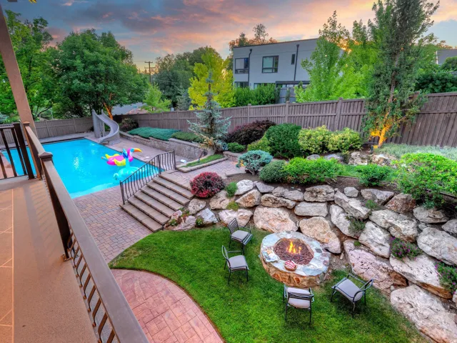 Expansive terraced backyard featuring a swimming pool with slide, paver patio, stone fire pit with seating, and a retaining wall with integrated landscaping
