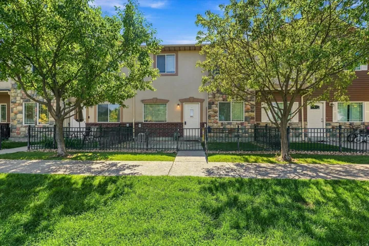 Stucco exterior with stone accents, wrought iron fencing, a mature tree, and a paved walkway