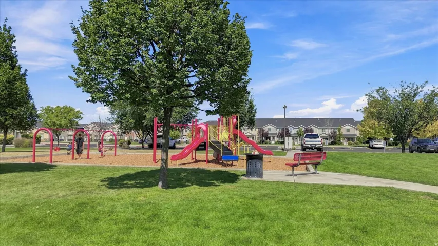 Expansive green space featuring a playground with swings and slides, mature trees, and a paved pathway