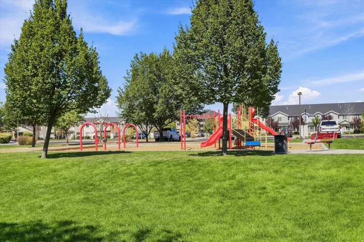 Expansive green space featuring a play structure with slides, swings, and a red bench