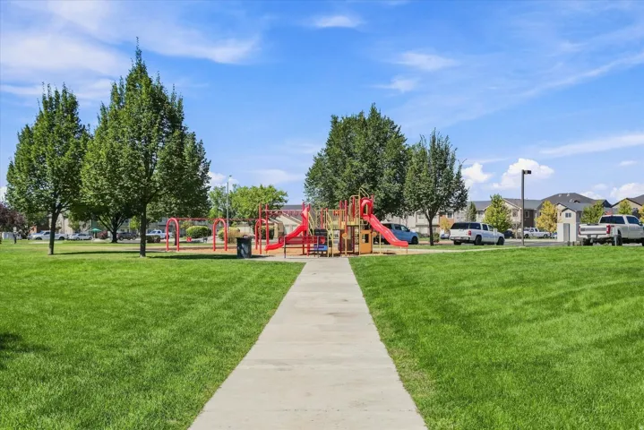 Expansive green space featuring a playground with slides and swings, mature trees, and a concrete pathway