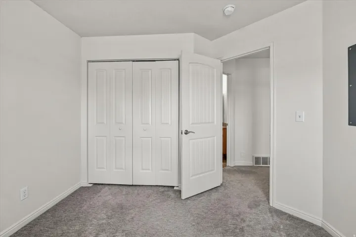Plush gray carpeting, white walls, white bi-fold closet doors, and white paneled door with brushed nickel hardware