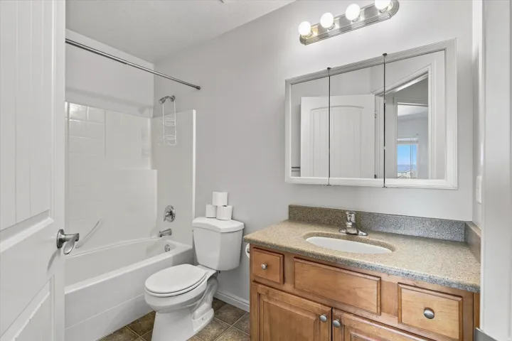Bathroom featuring a combination bathtub and shower with white tile surround, a single vanity with an integrated sink and light-toned countertop, and a mirrored medicine cabinet with overhead lighting