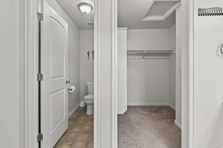 White interior door with arched paneling, overhead flush mount lighting, tiled flooring, and an open closet space with a single wire shelf