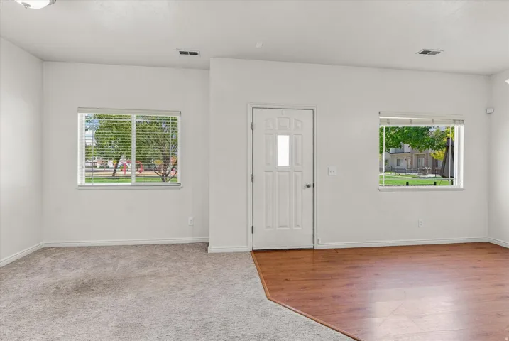 Entry area featuring wood-finish flooring, two windows with blinds, a white paneled door, and neutral wall tones