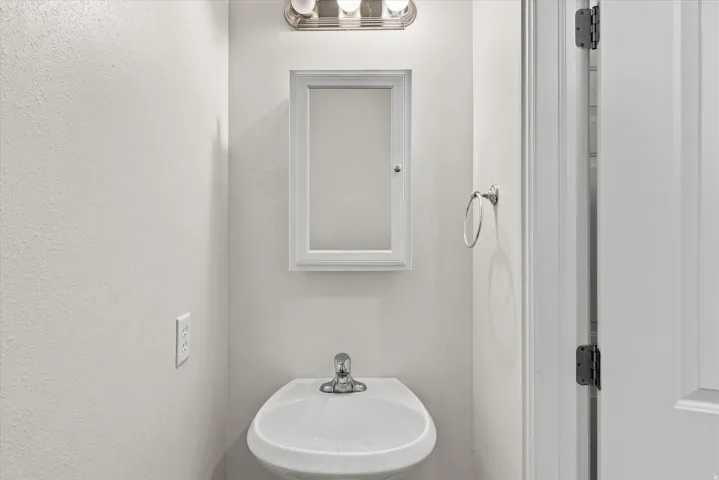 Pedestal sink with chrome faucet, framed medicine cabinet, and wall-mounted vanity light