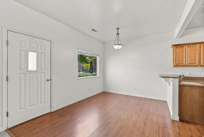 Wood-finish flooring, white paneled door with glass insert, natural light from exterior window, overhead pendant lighting, and a breakfast bar with built-in cabinetry