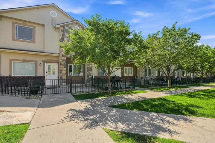 Multistory exterior with stone accents, a private gated patio, and a manicured lawn