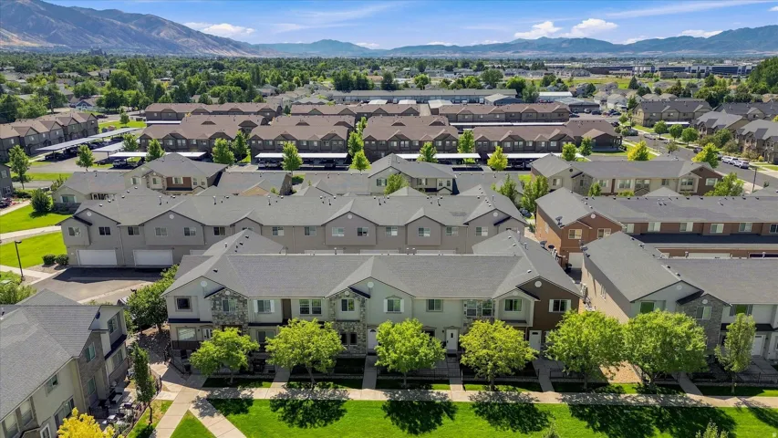 Community setting featuring multi-level townhomes with attached garages, mature landscaping, and mountain backdrop