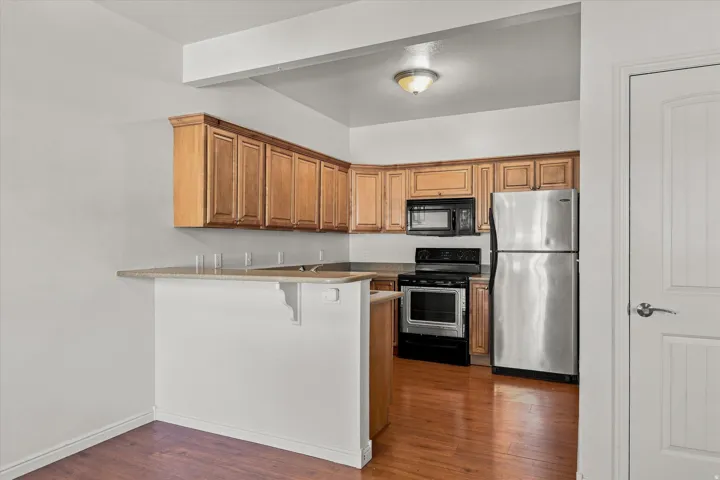 Kitchen featuring wood cabinetry, stainless steel refrigerator, black range, and black microwave