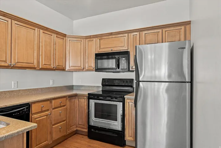 Wood-finish cabinetry, stainless steel refrigerator, black electric range, black microwave, and granite-look countertops