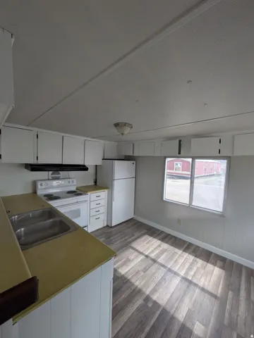 Kitchen featuring white cabinetry, wood-finish flooring, a double basin sink, and a two-pane window