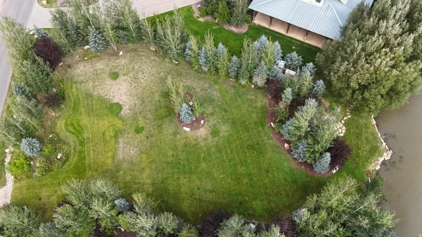 Expansive green lawn with diverse mature trees, bordering a natural water feature