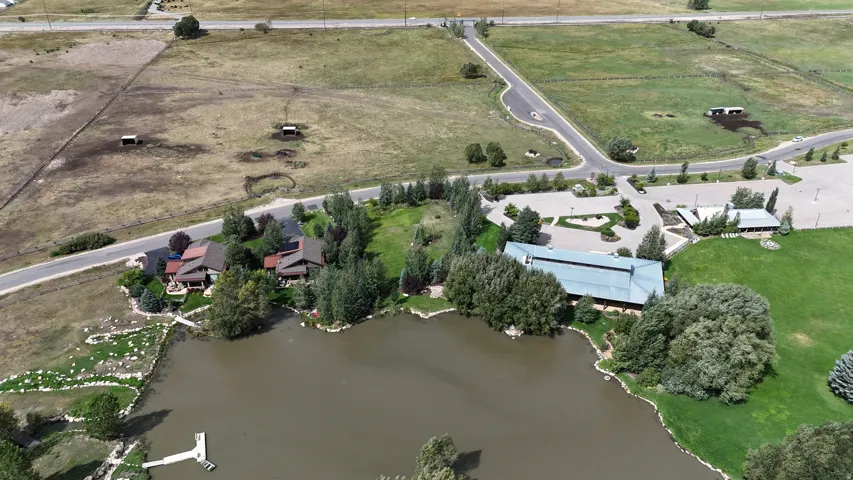Expansive property featuring a large body of water with a dock, surrounding green space, and mature trees