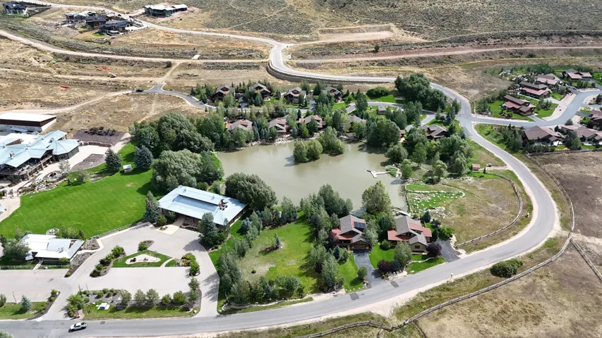 Expansive community featuring a central pond, surrounding residential structures, paved roadways, and mature trees