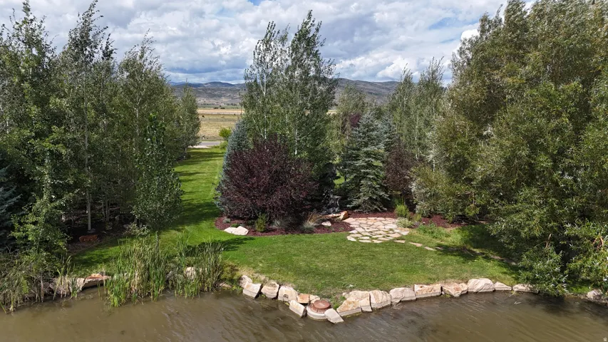 Waterfront landscaping with mature trees, a manicured lawn, and a stone patio