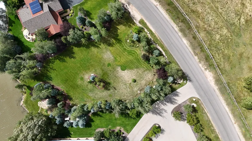 Expansive green lawn, mature trees, multi-level dwelling with solar panels, waterside access, and paved roadways