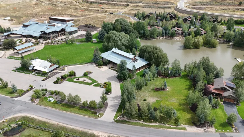 Expansive grounds featuring multiple buildings, paved parking areas, a body of water, and surrounding mature trees