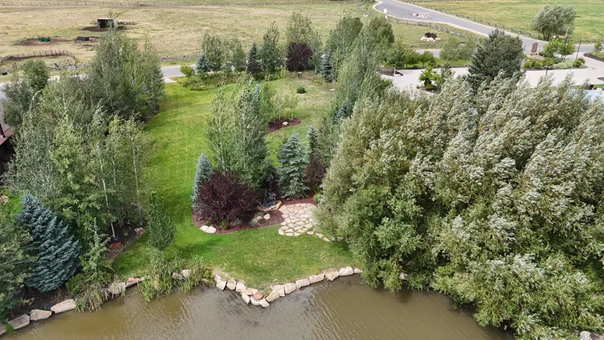 Manicured lawn with mature trees, a stone patio, and natural rock-lined pond