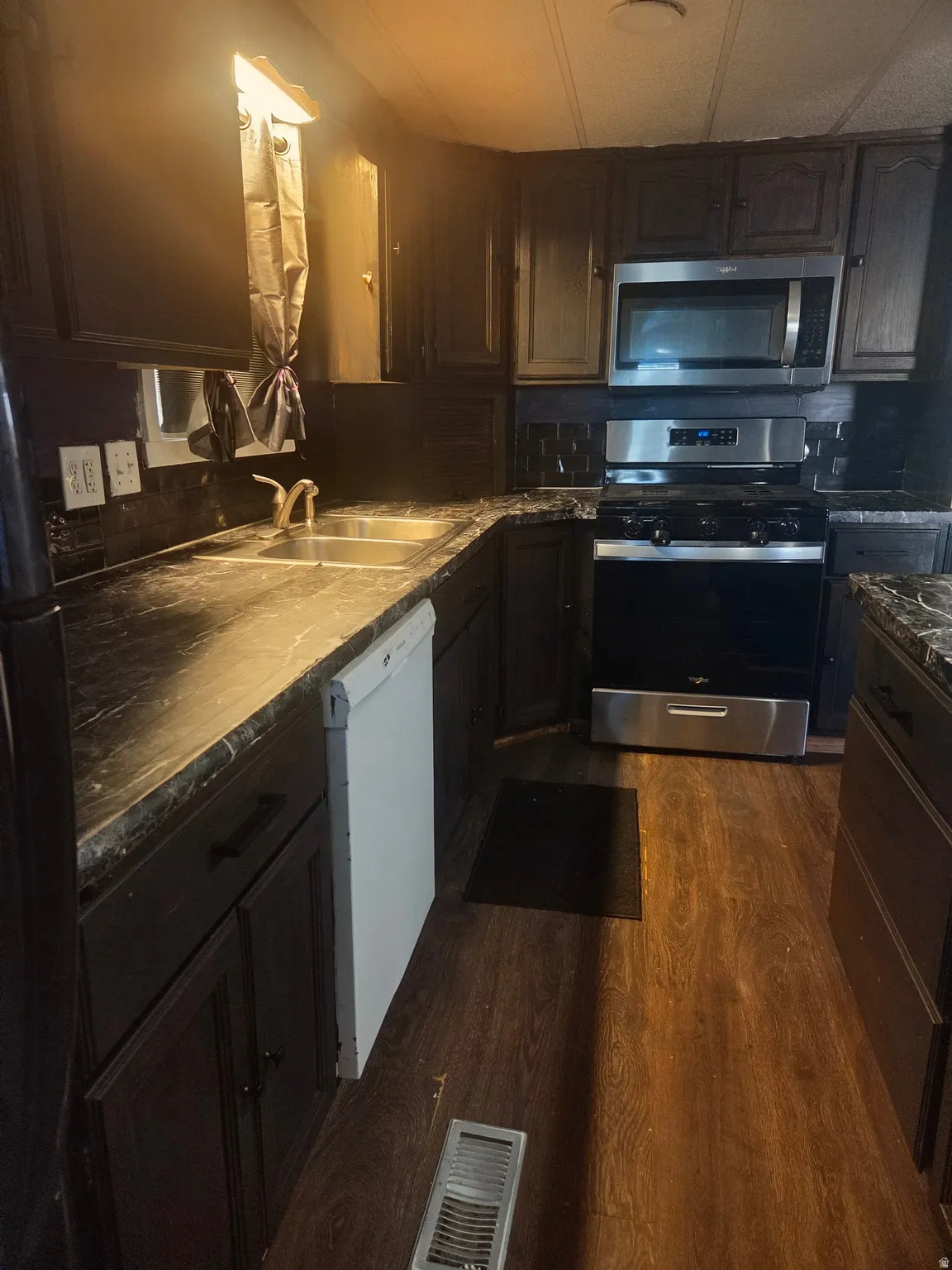 Kitchen featuring dark wood-finish cabinetry, stainless steel microwave, stainless steel range, and a double basin sink