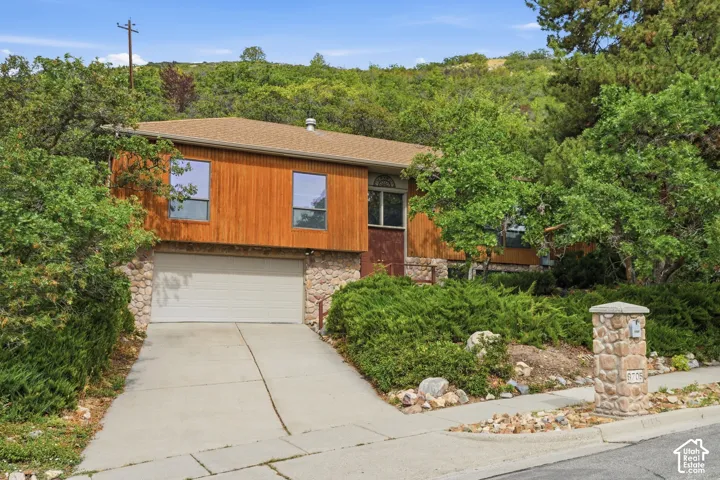 Wood-paneled facade with stone accents, a concrete driveway, and an integrated garage